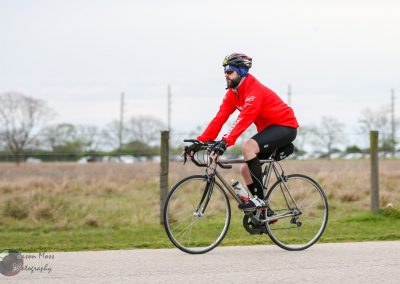 Man cycling outdoors wearing red jacket, black shorts, helmet, and sunglasses, promoting biking fitness and outdoor activity.