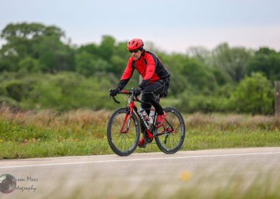 Vibrant cyclist riding a road bike in green countryside during daytime, promoting Bluebonnet Express cycling events.