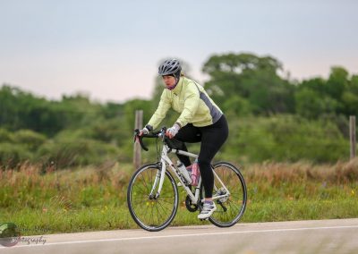 Bright woman cyclist riding on scenic countryside road, promoting outdoor biking with Bluebonnet Express.