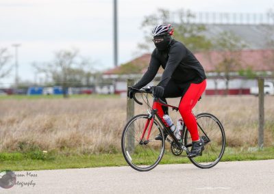 High-performance cyclist riding a red and black road bike outdoors on a cloudy day.