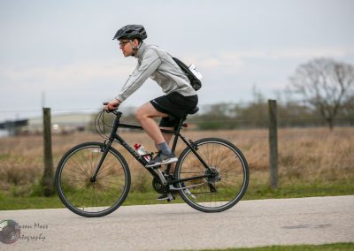 A man riding a black Trek bicycle on a rural road in overcast weather, participating in a cycling event.