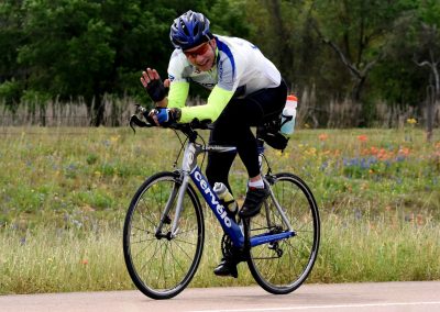 Vegan Bike Ride, cycling through scenic countryside, smiling cyclist waving at camera, Bluebonnet Express theme.