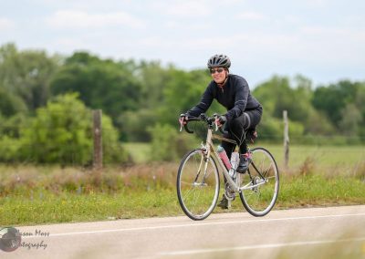 Vibrant woman cycling on scenic countryside road with greenery and blue sky.