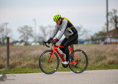 Vibrant orange Cervélo road bike with cyclist in gear on a paved path during daytime.