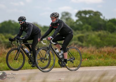High-performance cyclists riding on scenic open road with lush greenery in background.