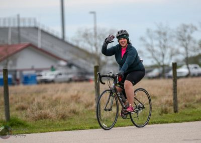 Smiling woman riding a blue bike outdoors, promoting Bluebonnet Express cycling event, active lifestyle, Texas scenery.