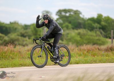 High-performance bike rider on scenic rural road, promoting Bluebonnet Express bike tours and cycling adventures.