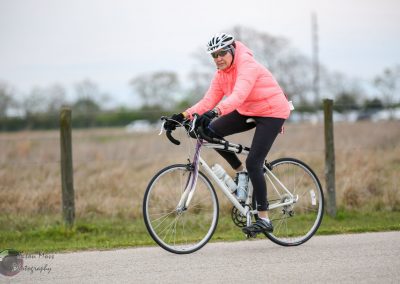 Bright woman cycling outdoors in pink jacket, black leggings, safety helmet, on a scenic bike trail.