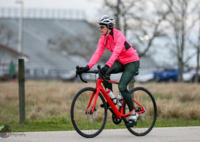 Bright pink athletic cycling jacket with black accents on a woman riding a red bike for Bluebonnet Express.
