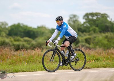 Vibrant cyclist riding a black bike on scenic Texas countryside road, promoting Bluebonnet Express cycling tours.