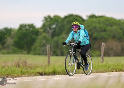 Bright woman cycling outdoors wearing a blue jacket and helmet on a scenic trail for eco-friendly transportation.