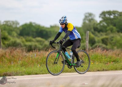 Bright cyclist riding a green and black road bike on open countryside during daytime.