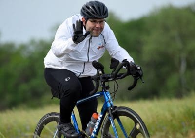 Vibrant cyclist waving on a scenic outdoor trail with a blue bike, showcasing active lifestyle and bike commuting.