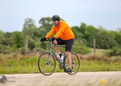 Bright orange jacket cyclist riding on scenic rural road during daytime.