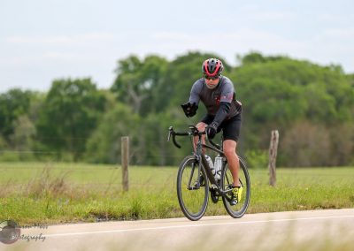 Vast open road with a cyclist riding a black bike in a rural area during daytime.
