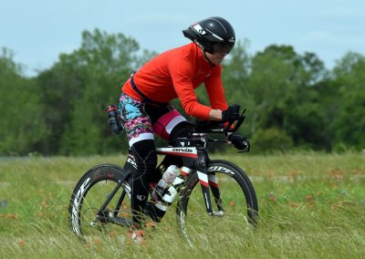 Vibrant cyclist riding a professional bike through a grassy field with trees in the background.