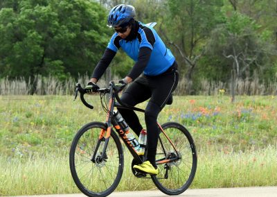 Vibrant cyclist on a mountain bike riding through scenic fields with wildflowers and green trees, highlighting outdoor biking adventures.