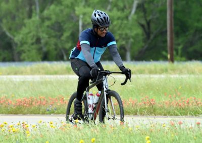 Bright blue mountain bike riding through scenic wildflower fields on a lush green bike trail.