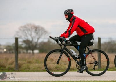 Vigorous cyclist in red and black biking gear on a scenic outdoor route during daytime.