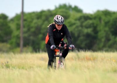 Rider cycling on a scenic trail with lush green trees in the background.