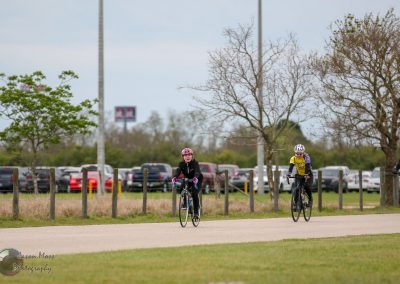 Brightly colored bicycles riding along a park trail during daytime with trees and parking lot background.