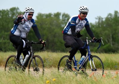 Cyclists wearing Bluebonnet Express jerseys riding mountain bikes outdoors in a grassy field.