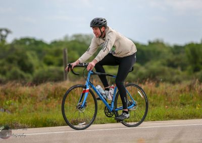 Bright blue Bluebonnet Express road bike with rider in cycling gear on open road during daytime.