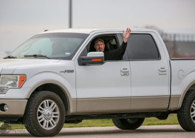 Man waving from a white pickup truck on a road, promoting Bluebonnet Express bike transportation service.