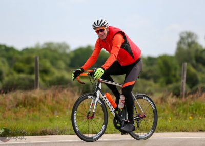 Vibrant cyclist riding a road bike on open countryside, promoting Bluebonnet Express cycling service.