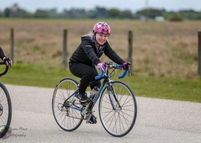 Bright young woman cycling outdoors on scenic bike path, promoting Bluebonnet Express cycling event.
