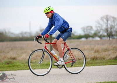 Senior cyclist riding a red road bike outdoors, enjoying a scenic ride on a cloudy day.