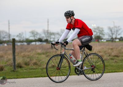 Cyclist riding a road bike outdoors on a cloudy day, promoting Bluebonnet Express cycling services.