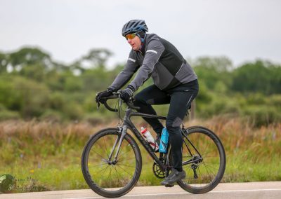 Bright male cyclist riding a road bike in outdoor scenery for Bluebonnet Express event.