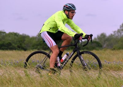 Bright yellow cyclist jacket, black helmet, riding Cannondale bike on grassy trail.
