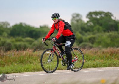 Bright red biking jacket for women cycling in open countryside during Bluebonnet Express event.