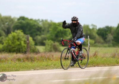 Bright cyclist in black gear and colorful shorts waving on scenic road.