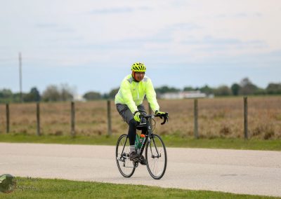 Bright cyclist riding on a bike path outdoors in a rural area during daytime.