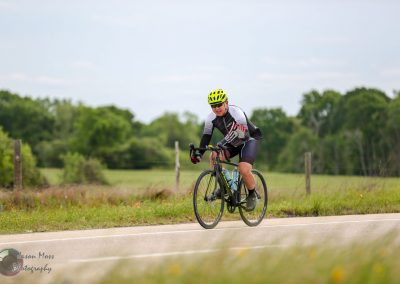 Vibrant cyclist riding a black bike along a scenic rural road in Texas with lush greenery in the background.