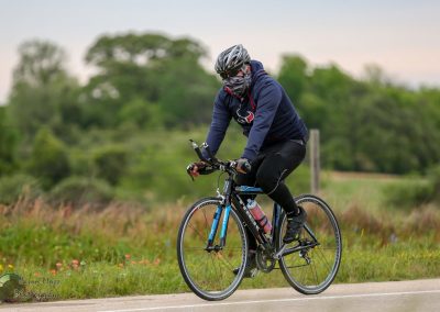 Bright blue bike with rider wearing hoodie, helmet, and mask on scenic outdoor trail.