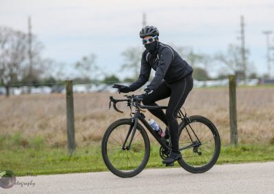 Bright blue-tinted sunglasses and a face mask complete a cyclist's black athleisure gear on a scenic bike ride.