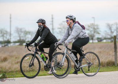 Vegan women and man riding bikes outdoors on paved trail, wearing helmets, casual athletic gear, and smiling.