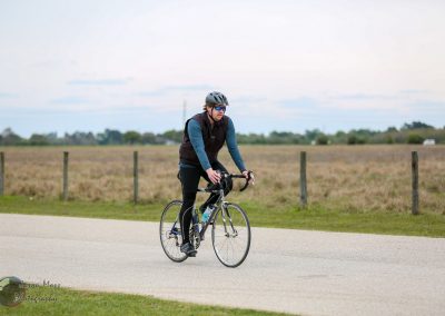 Cyclist riding a bike in open countryside with bluebonnet express branding in the background.