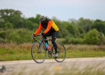 High-performance cyclist riding a road bike on scenic rural trail for Bluebonnet Express.