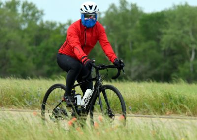 Bright red jacket cyclist wearing helmet and face mask riding a mountain bike outdoors in green field.