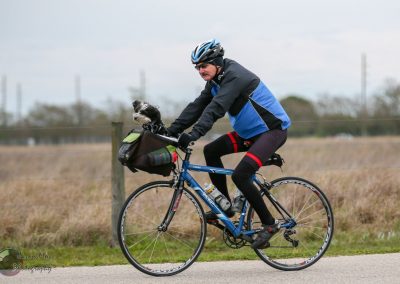Cyclist riding a blue bike with a dog in a front handlebar bag - Bluebonnet Express.