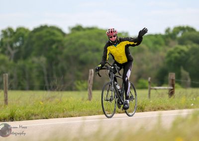 Cyclist waving on scenic rural road, promoting Bluebonnet Express bike services.