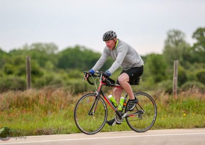 Vibrant cyclist riding on scenic road with greenery and bluebonnets, promoting Bluebonnet Express bike tour.
