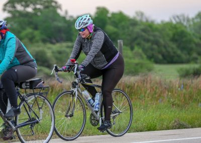 Colorful cyclists riding on a scenic trail during daytime, promoting Bluebonnet Express biking events.