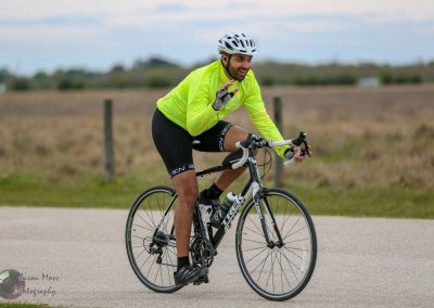 Vegan cyclist waving while riding a road bike in an open countryside scene.