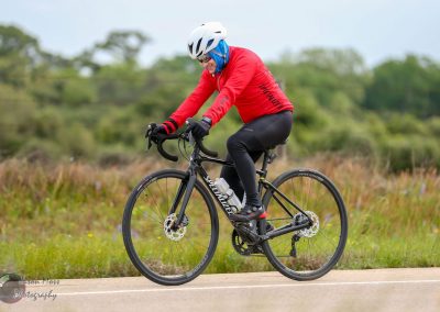 Vibrant cyclist riding a black road bike on a scenic trail, promoting Bluebonnet Express cycling tours.